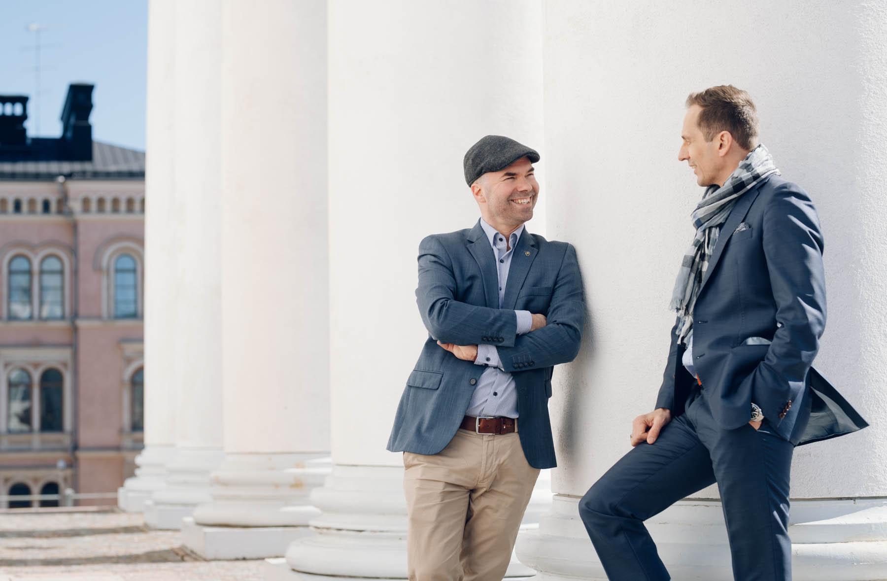Kaksi miestä keskustelee hymyillen Helsingin Tuomiokirkon edustalla.